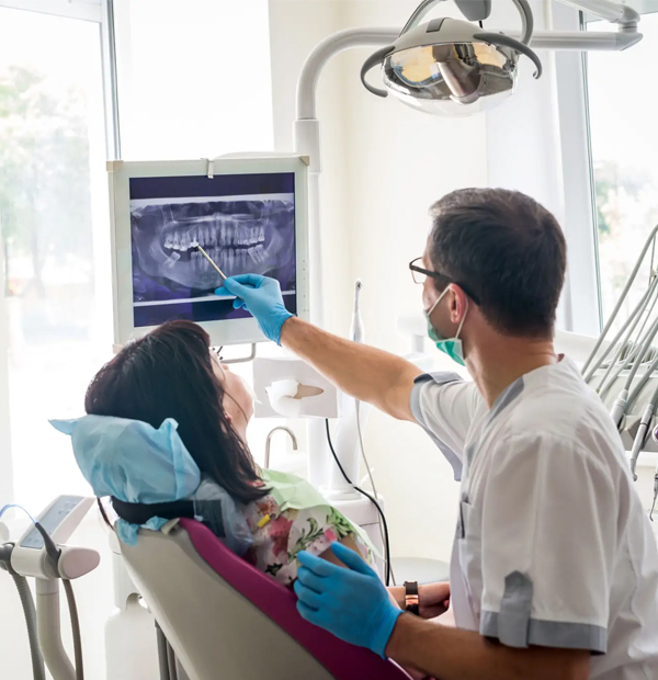Dentist examining patient's dental X-ray on monitor in modern dental clinic operatory.