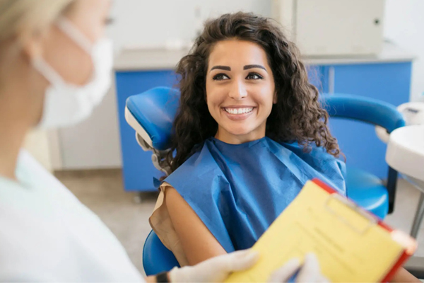 Female patient wearing blue bib smiling at dentist in dental office treatment room.
