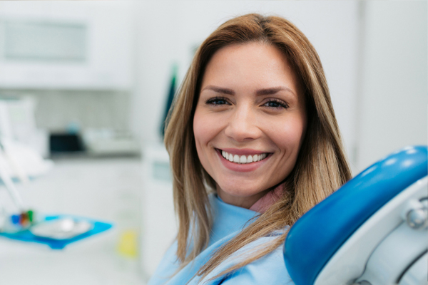 Smiling woman in dental office with blue equipment, professional dental care setting.
