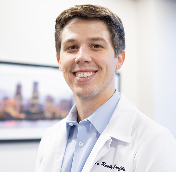Male dentist in white coat and blue shirt smiling in dental office