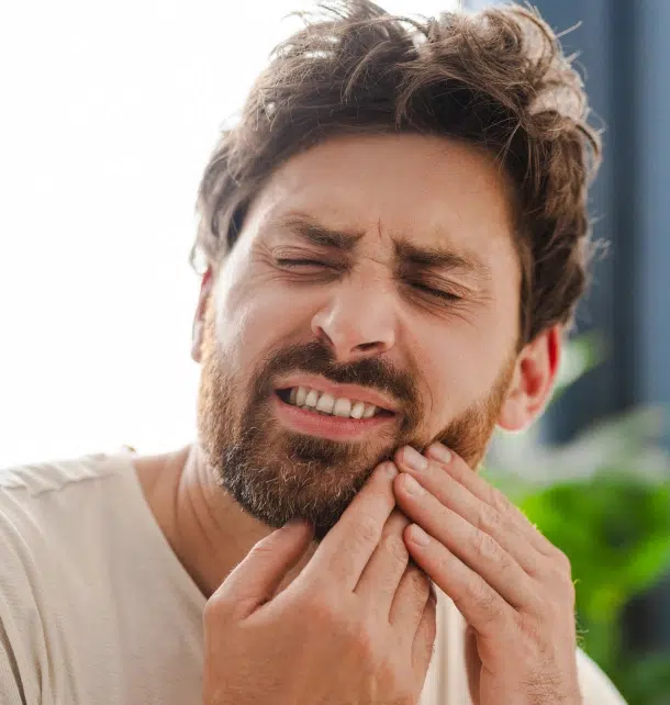 Man holding jaw in pain, outdoors, suggesting dental discomfort or toothache