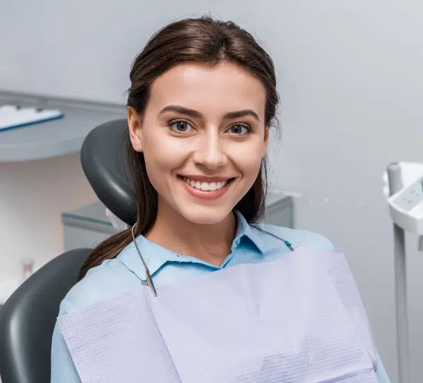 Smiling dental professional in light blue uniform sitting in dental office chair.