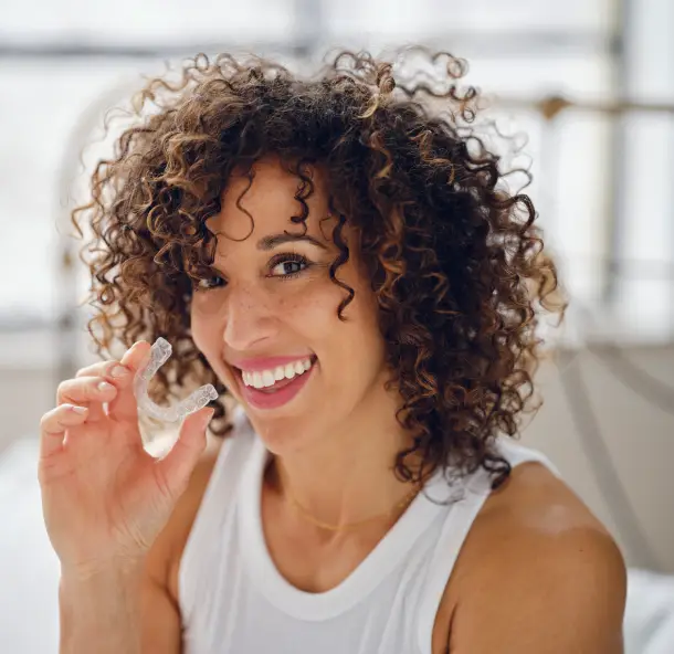 Woman with curly hair smiling while holding dental floss in bright, modern dental office setting.